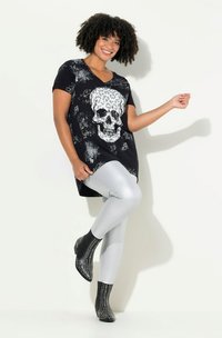 Černá tunika s bílým lebkovým potiskem leopardího vzoru, doplněná lesklými stříbrnými legínami a kotníkovými botami s hřebíkovými akcenty.