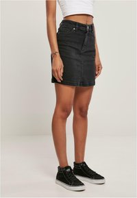 Zwarte denim rok met een aansluitende vorm, voorzien van voorzakken, een knoopsluiting en omgezoomde randen, gecombineerd met zwarte hoge sneakers.