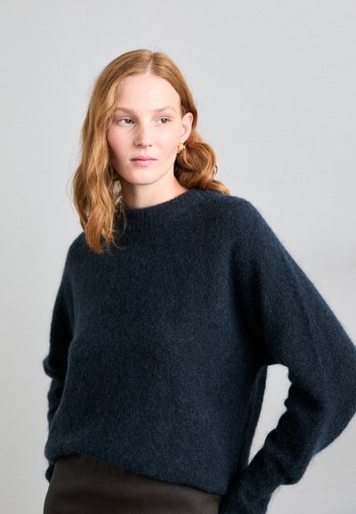 Pull en laine doux, bleu marine, avec un col rond, des épaules tombantes et des poignets côtelés. Texture lisse avec une coupe décontractée.