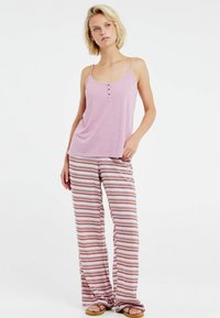 Lichtroze hemdtop met verstelbare bandjes en knoopaccenten, gecombineerd met gestreepte, wijde broek met zigzagpatroon in aardetinten.