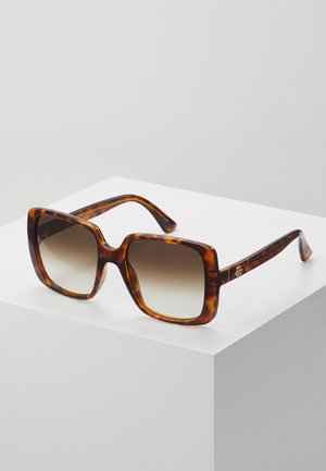 Lunettes de soleil en écaille avec une monture carrée épaisse, des verres dégradés et un subtil matériel doré sur les branches. Design de surface texturé.