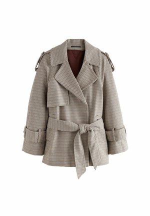 Person iført en ternet oversized blazer med bælte, mørke vide jeans og en lys top mod en ensfarvet brun baggrund.