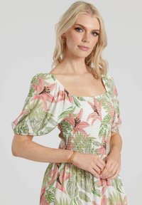 Blommig klänning med fyrkantig halsringning, puffärmar, vit tyg med rosa och gröna botaniska tryck samt smockdetaljer vid bysten.