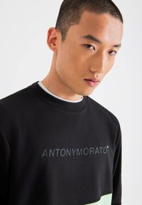Sudadera negra con cuello redondo y acentos en verde. Presenta el logo de la marca "ANTONY MORATO" en relieve en el pecho. Textura suave.