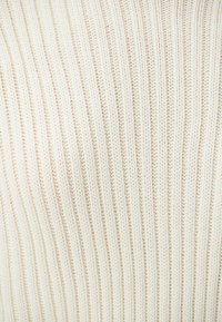 Strickpullover in Cremefarbe mit vertikalem Rippenmuster, das eine weiche Textur und eine figurbetonte Form zeigt.