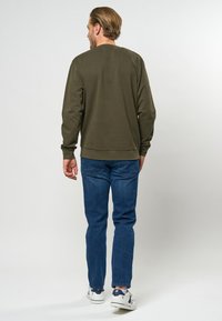 Olijfgroene sweatshirt met een ronde hals, lange mouwen en geribbelde boorden, gecombineerd met blauwe jeans en witte sneakers. Eenvoudig en casual ontwerp.