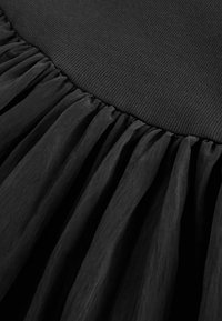 Gros plan d'un tissu noir avec une ceinture en maille côtelée et un tissu de jupe transparent et froncé en dessous.