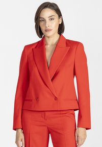 Czerwona, dopasowana marynarka z dwurzędowym zapięciem, ostrymi klapami i gładką fakturą; zestawiona z pasującymi czerwonymi spodniami.