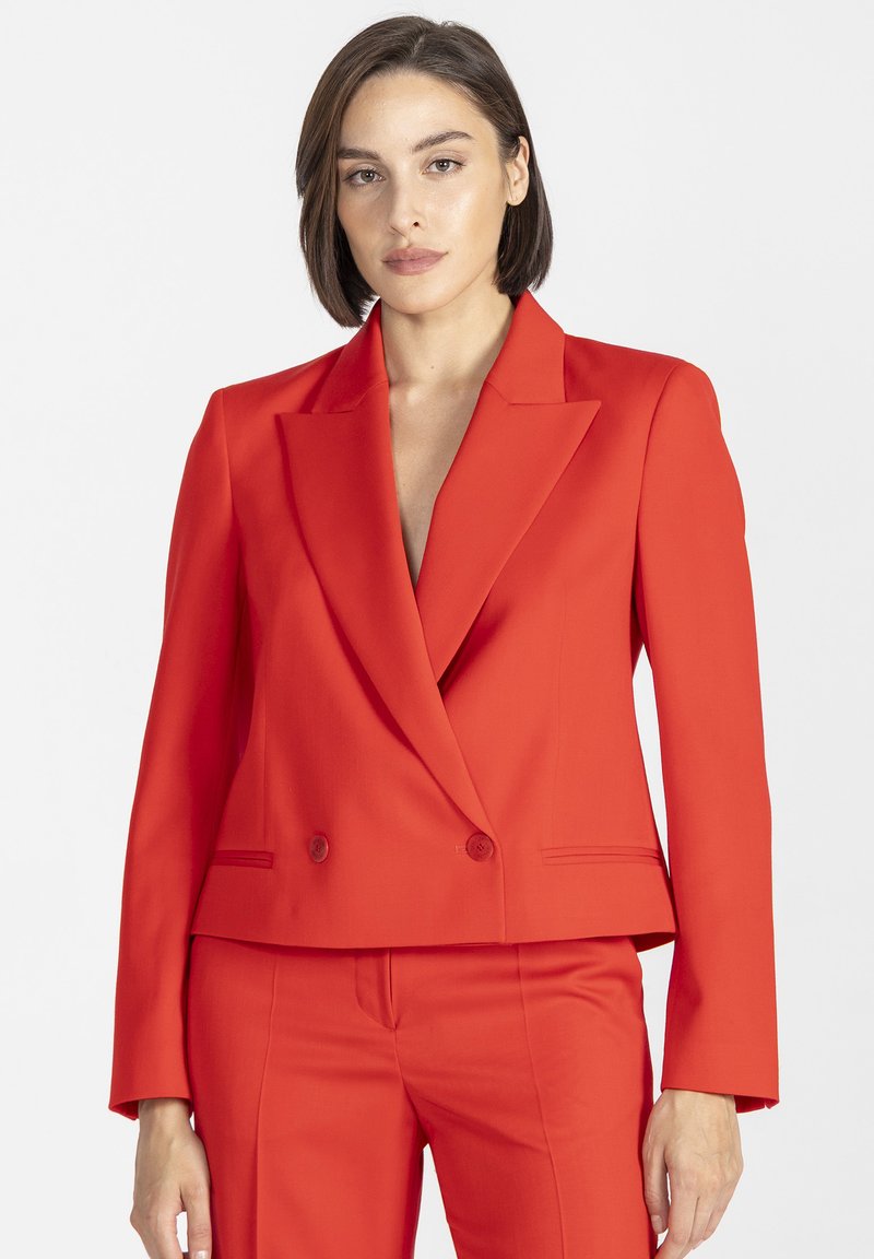 Czerwona, dopasowana marynarka z dwurzędowym zapięciem, ostrymi klapami i gładką fakturą; zestawiona z pasującymi czerwonymi spodniami.