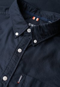 Marineblauw overhemd met knopen, voorzien van een gestructureerde kraag, witte knopen en een klein logo label. Gemaakt van gladde stof met een subtiele textuur.