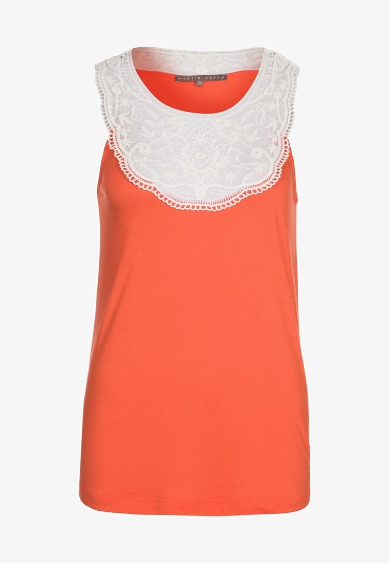 Haut orange sans manches avec encolure ronde et plastron en dentelle blanche décoré de broderies florales et de bords festonnés.