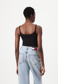 Top tank nero a coste con spalline sottili, abbinato a jeans a gamba larga di un blu chiaro con etichetta di marca sul retro.