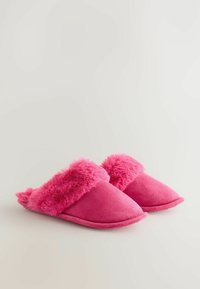 Różowe kapcie z miękkim sztucznym futerkiem przy kołnierzu i gładkim zamszowym wykończeniem. Charakteryzują się przytulnym designem z zaokrąglonymi palcami i płaską podeszwą.