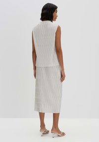 Sleeveless pleated top and midi skirt set in light gray, featuring vertical stripes, smooth texture, and subtle sheen. Silver heeled sandals.