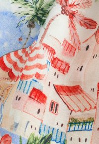 Tissu imprimé avec un village en bord de mer coloré, comprenant des maisons aux toits rouges, des auvents bleus, des palmiers verts et un ciel dégagé.