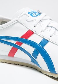 Hvide lædersneakers med blå og røde striber, snørebåndslukning, tekstureret overflade og en beige gummisål med branding på tungen.