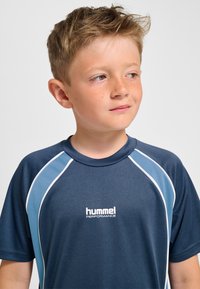 Marineblå sportt-shirt med ljusblå detaljer och vit kantning. Har rund halsringning och "hummel PERFORMANCE"-märke på framsidan.