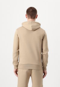 Felpa beige realizzata in morbido tessuto, dotata di un ampio cappuccio, polsini a costine e orlo dritto. Design semplice senza motivi o decorazioni visibili.