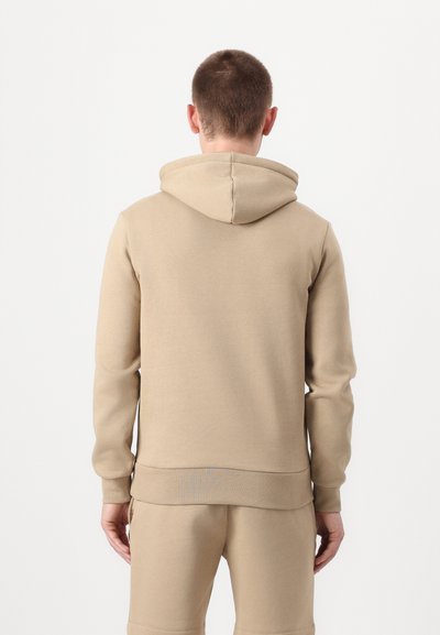 Hoodie beige en tissu doux, doté d'une grande capuche, de poignets côtelés et d'un ourlet droit. Design simple sans motifs ni accents visibles.