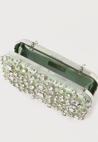 Zelená saténová kabelka s kovovým rámem ve stříbrné barvě, zdobená různými jasnými drahokamy ve složitých vzorech a měkkou podšívkou.