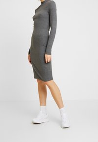 Abito grigio a coste con maniche lunghe e collo alto, silhouette aderente, lunghezza al ginocchio, abbinato a sneakers bianche e calze.