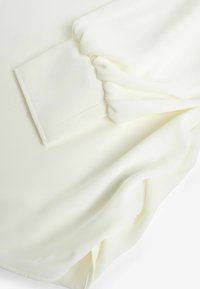 Hvid bluse i letvægtsstof, med detaljer i form af samlede ærmer og glat tekstur. Enkel design med et rent finish.