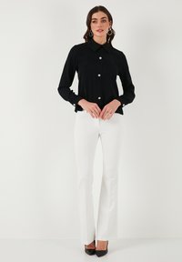 Black long-sleeve shirt with a collar, featuring shiny buttons down the front. Paired with white flared trousers and black high heels.
