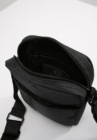 Black textured fabric shoulder bag with zip closure, adjustable strap, and multiple inner compartments for organization. Reflective accents present.