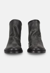 Botas negras hasta el tobillo hechas de cuero perforado, con una textura suave, punta redondeada y suela plana. Diseño minimalista sin herrajes visibles.