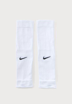 Paire de manchons de sport blancs avec logos Nike Swoosh noirs sur un fond clair uni, posés à plat côte à côte.