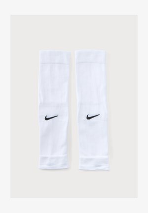 Valgete spordivarrukate paar mustade Nike Swoosh logodega lihtsal heledal taustal, kõrvuti tasaselt laotuna.