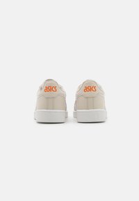 Beige lädersneakers med vita accenter, med en texturerad design och orange "ASICS"-logotyp på hälen. Helt vit gummisula.