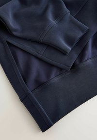 Marineblå sports sweatshirt med glat stof, lagdelte lag og ribbet kant, med syningsdetaljer på ærmekanter og sømme.