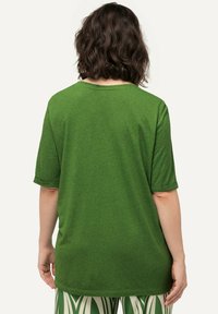 Camiseta verde de manga corta hecha de un tejido texturizado, con un corte holgado y mangas enrolladas, vista desde la parte de atrás.