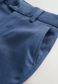 Tumesinised kohandatud püksid tekstuurse kangaga, millel on nööbiga sulgur, vööaugud ja korralikult õmmeldud õmblused.