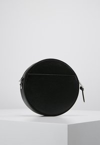 Borsa rotonda nera in pelle con finitura texture e zip in metallo silver. Presenta un design minimalista e una base piatta per maggiore stabilità.