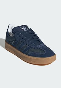 Sneakers blu navy con tomaia in suede e denim, patch del logo bianco e suola in gomma color caramello. Presentano tre accenti a strisce e dettagli testurizzati.