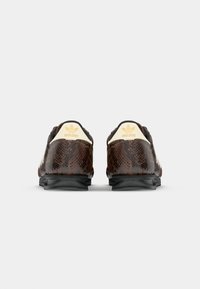 Sneaker in pelle di serpente marrone, strutturata, con suola nera e linguetta del tallone crema con logo Adidas dorato. Stile distintivo con motivi intricati.