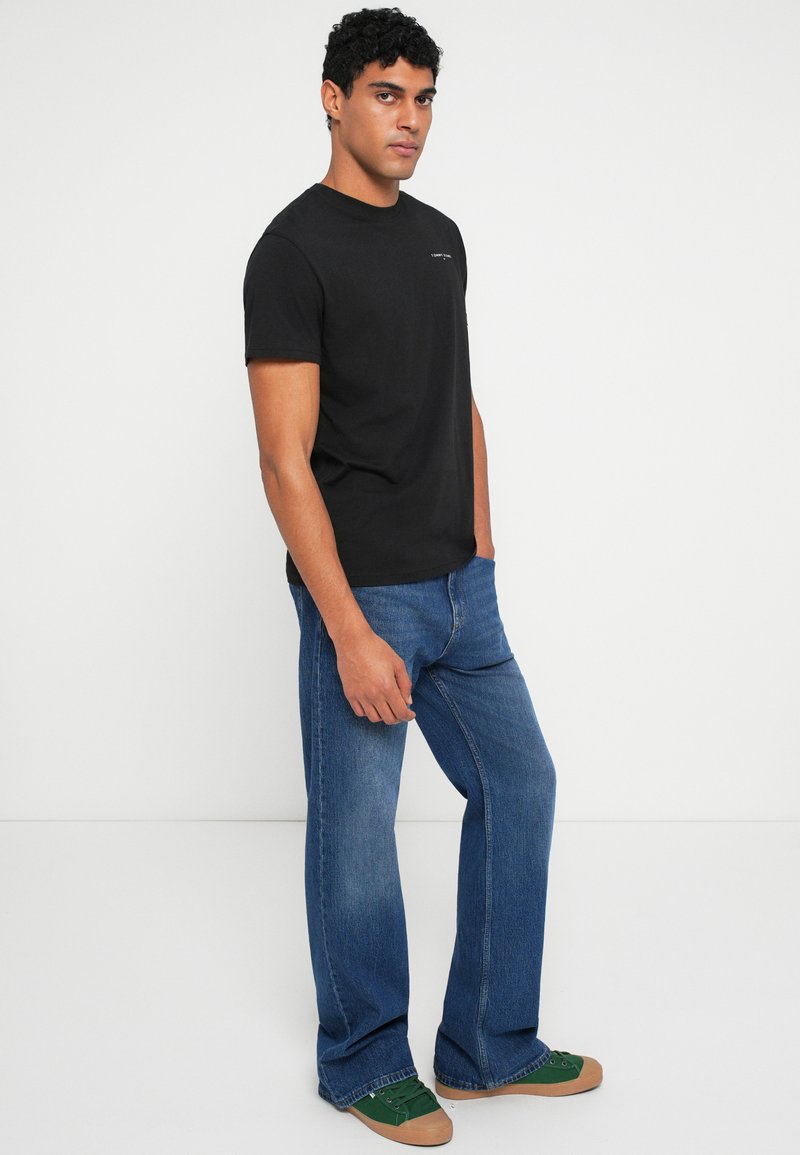 Sort bomulds T-shirt med korte ærmer og rund hals, parret med lyseblå flagrende denimjeans og grønne sneakers med brune såler.