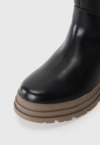 Bottine noire en cuir avec un bout arrondi et une semelle en caoutchouc marron texturée dotée de profondes rainures pour une meilleure traction.