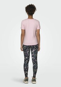 Camiseta de manga corta rosa claro combinada con leggins oscuros de flores con patrones en blanco, rosa y verde, complementada con zapatillas verde oliva.