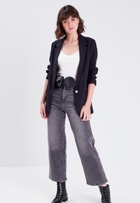 Black blazer with structured shoulders, white lace tank top, gray wide-leg jeans, and a black croc-textured belt. Black lace-up boots.