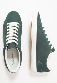 Baskets en textile vert avec lacets blancs et semelle en caoutchouc. Elles présentent une tige texturée et une doublure blanche contrastante le long du col.