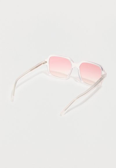 Τετράγωνα, διάφανα γυαλιά ηλίου με φακούς σε ροζ διαβάθμιση, ανοιχτά πάνω σε λευκή επιφάνεια.