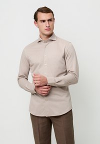 Lichtbeige overhemd met lange mouwen, puntkraag, knoopsluiting aan de voorkant en rechte zoom. Glad materiaal, gecombineerd met kaki broek.