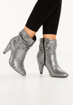 Enkellange zilveren glitterlaarzen met puntige neuzen, gestapelde hakken, nonchalante textuur, zijrits, gedragen met zwarte nauwsluitende broek.
