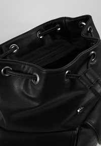 Czarna skórzana torba-bucket z srebrnymi oczkami, sznurkiem do zaciągania i wewnętrzną kieszenią na zamek. Miękka tekstura i przestronny design.