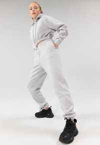 Sweat à capuche gris clair court avec taille élastique, associé à un pantalon de jogging assorti avec poches latérales et poignets élastiques, complété par des baskets noires.