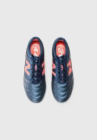 Zapatillas deportivas azul marino con un upper de cuero texturizado, que presenta un audaz logo "N" en rosa y un diseño de plantilla con rayas rojas.