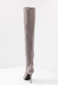 Bota gris de ante por encima de la rodilla con puntera afilada y tacón de aguja. Presenta un cierre lateral para facilitar su uso. Textura suave en toda la bota.